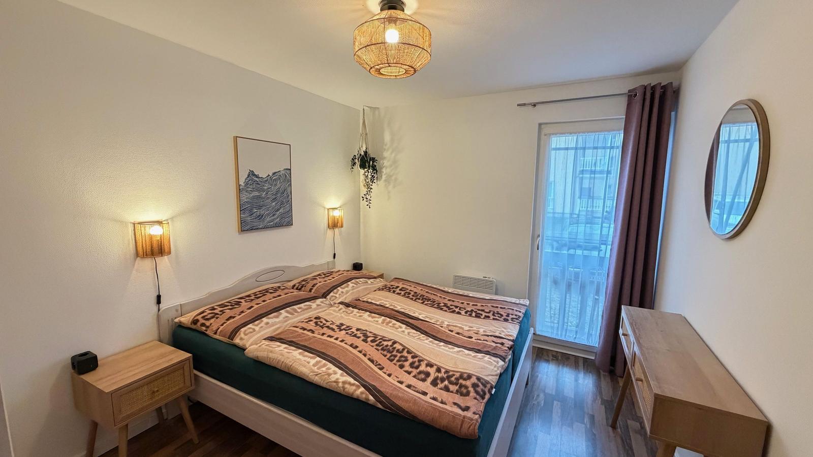 Schlafzimmer mit Bett, Nachttisch, Schreibtisch und Balkontür.