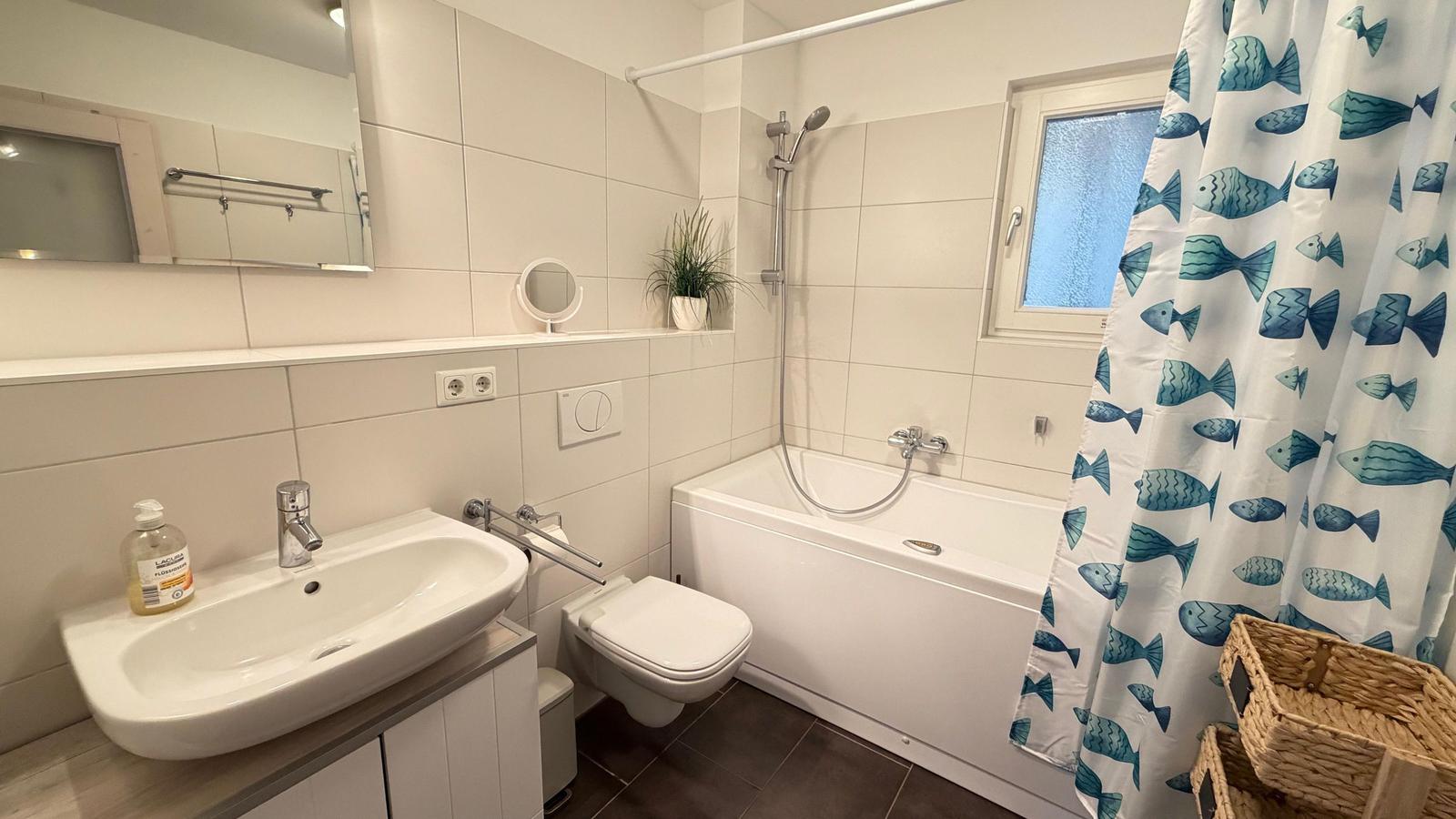 Badezimmer mit Badewanne, Dusche, Waschbecken und Fischmuster-Duschvorhang.