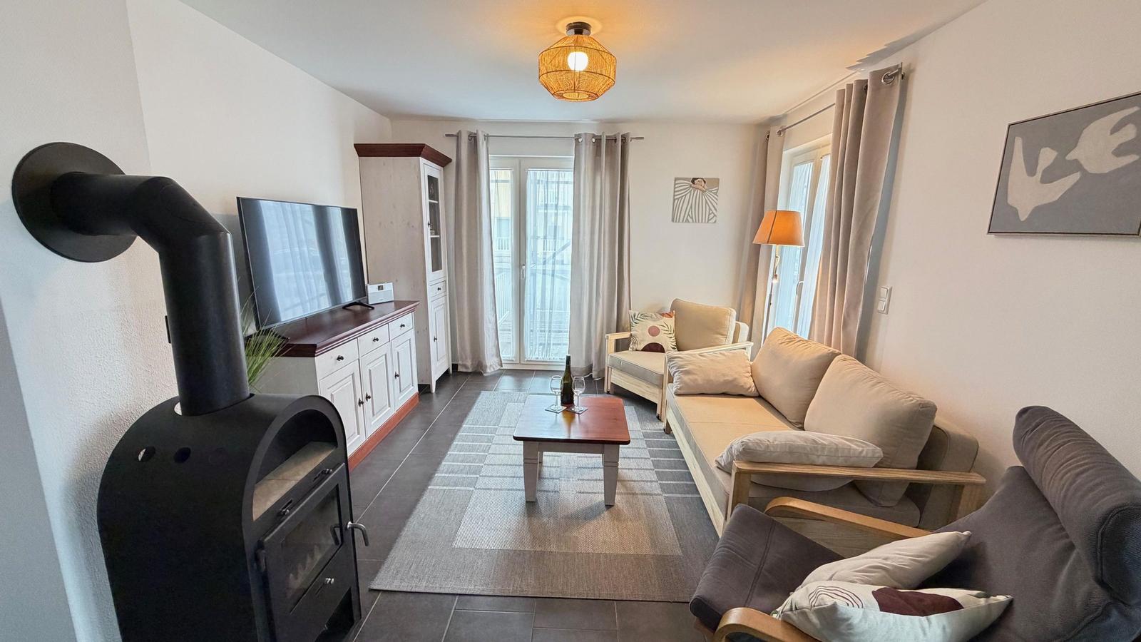 Wohnzimmer mit Sofa, Couchtisch und Kaminofen. Fenster mit Blick auf Balkon.