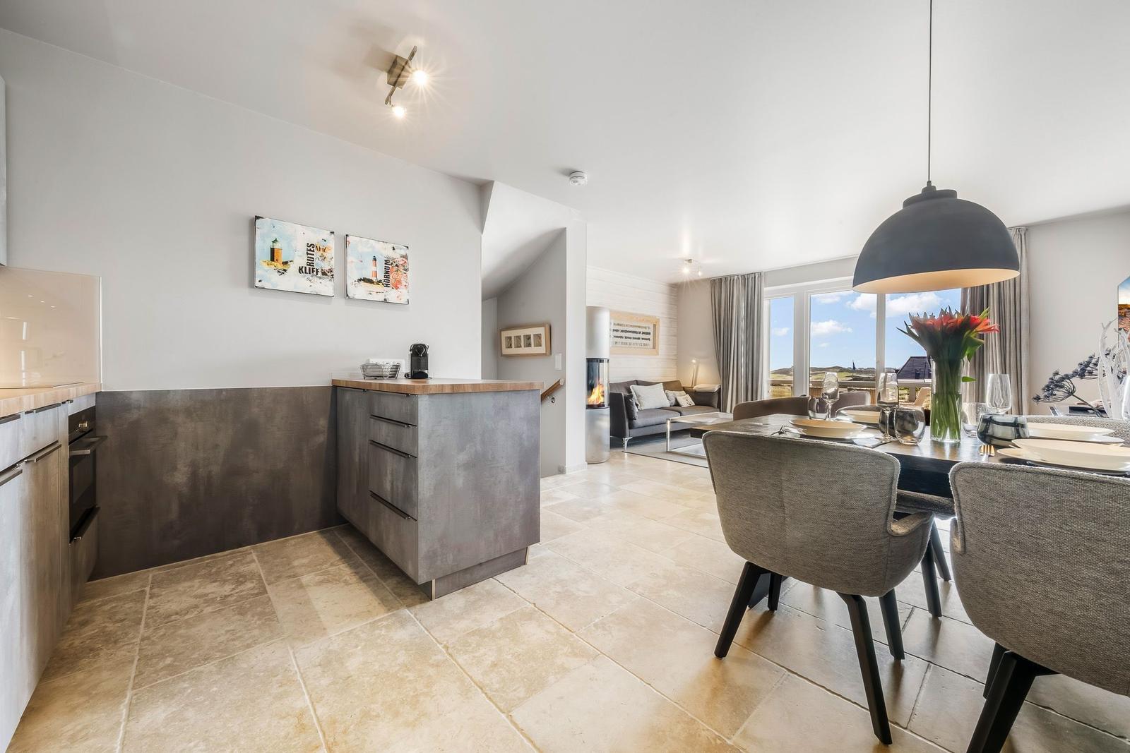 Küche mit Essbereich und Wohnzimmer im Hintergrund. Große Fenster mit Blick auf Landschaft.