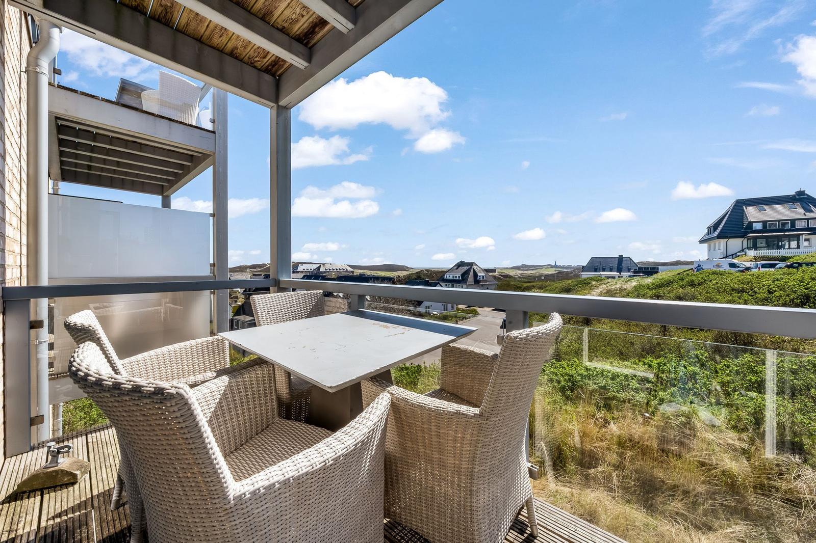 Terrasse mit Tisch und Stühlen, Blick auf Dörfer und Grünflächen unter blauem Himmel.