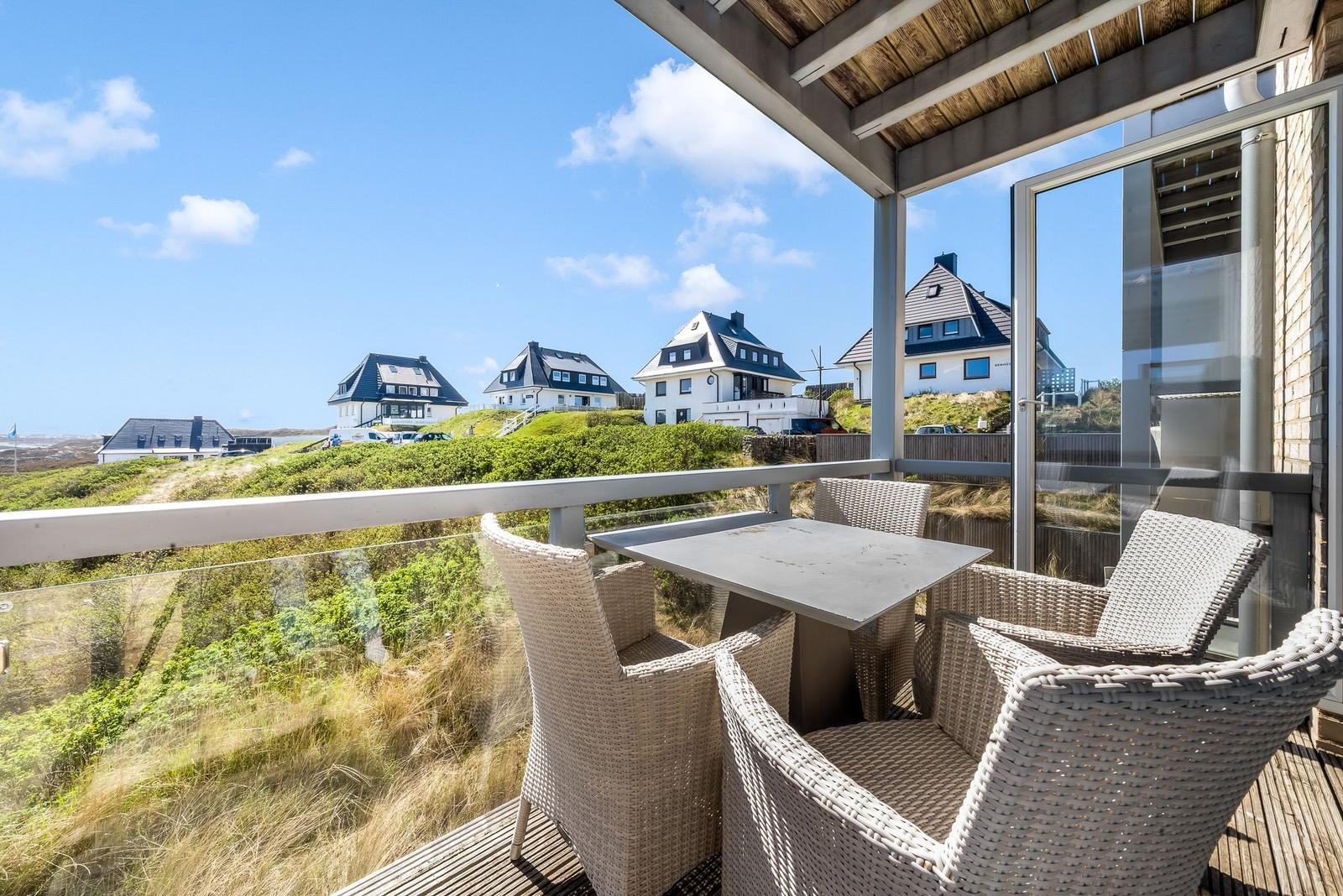 Terrasse mit Tisch und Stühlen, Blick auf Häuser und Grünland unter blauem Himmel.