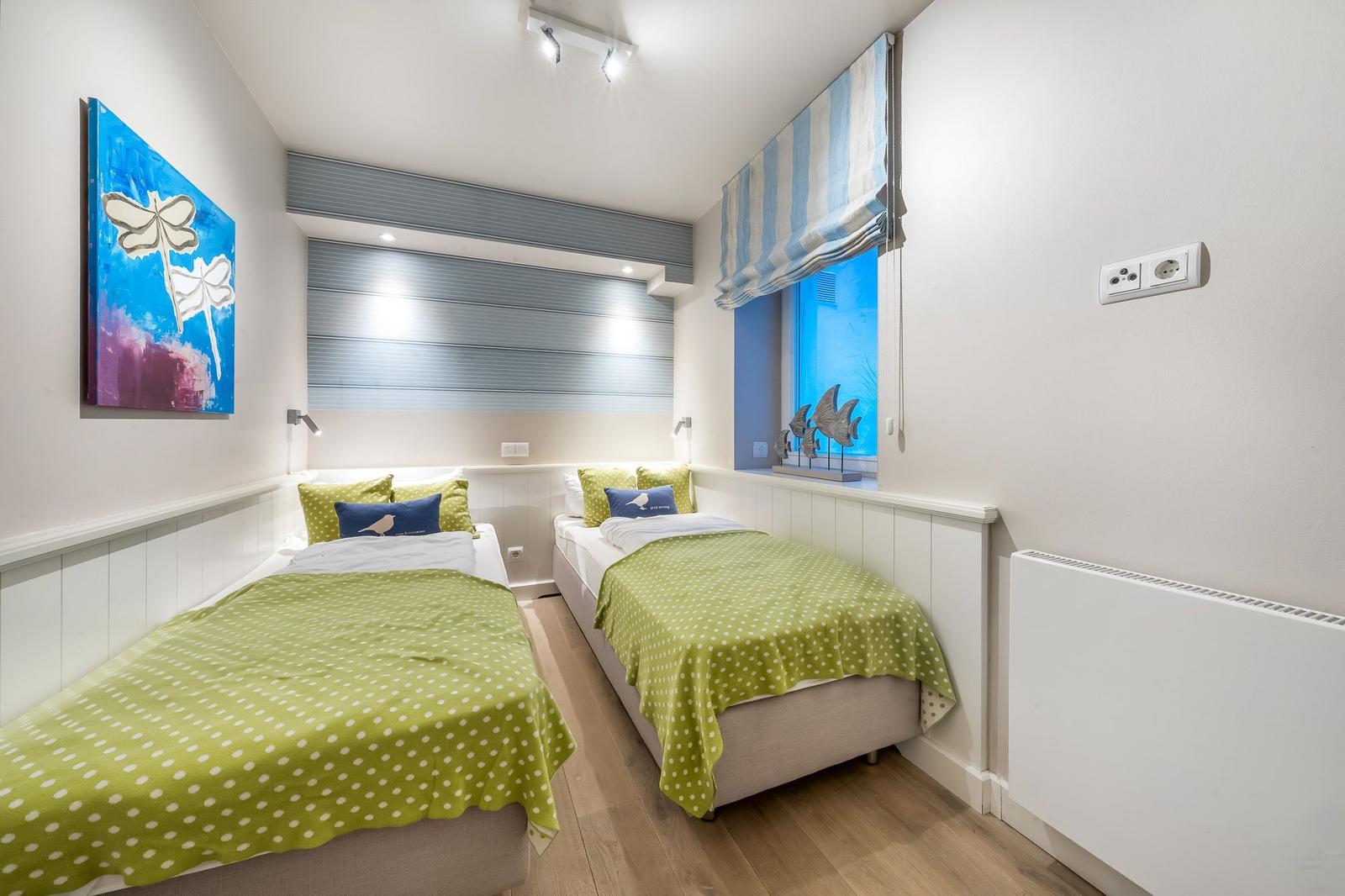 Zwei Einzelbetten mit grünen Decken, Wandbild und Fenster mit Rollladen.
