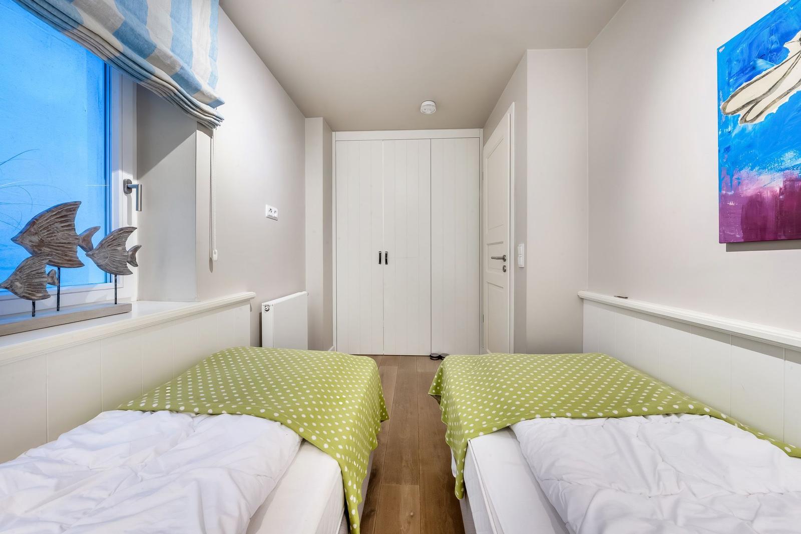 Zwei Betten mit grünem Deckenbezug stehen in einem Raum mit Fenster und Wandbild.