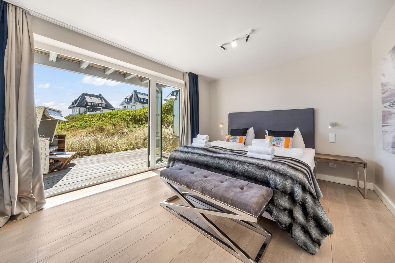 Schlafzimmer mit Blick auf Terrasse und Grünfläche. Bett mit Decke und Kissen.