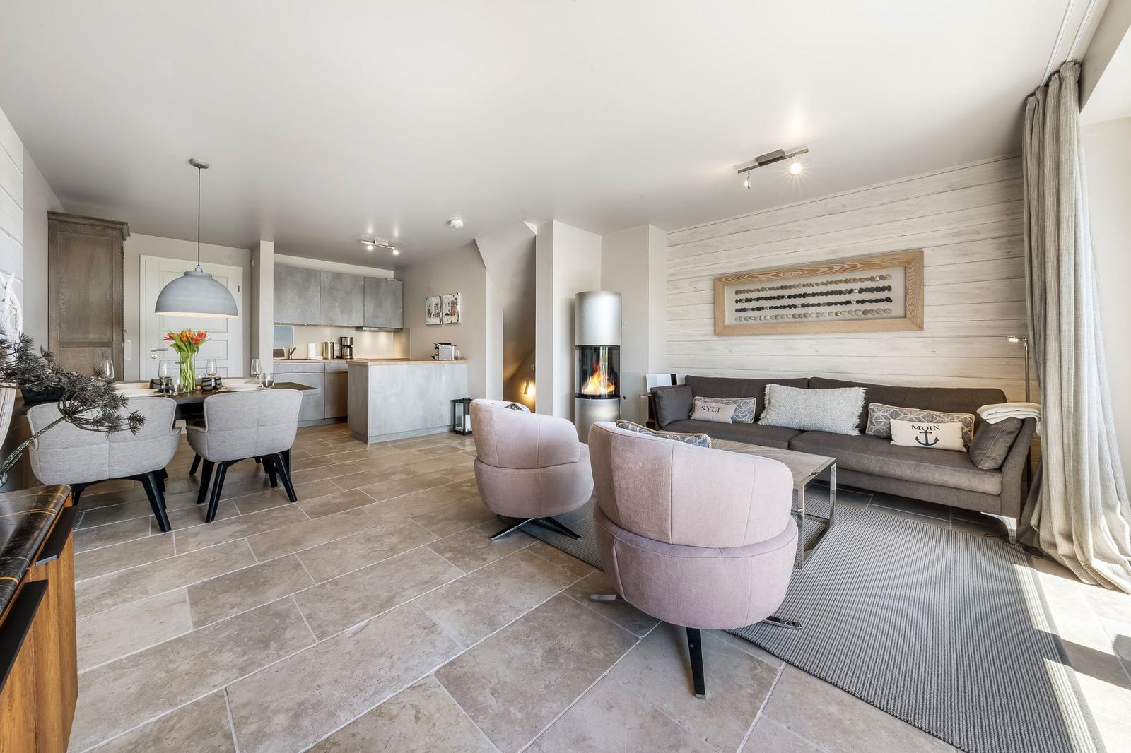 Wohn- und Essbereich mit Sofa, Sesseln und Kamin. Küche im Hintergrund.