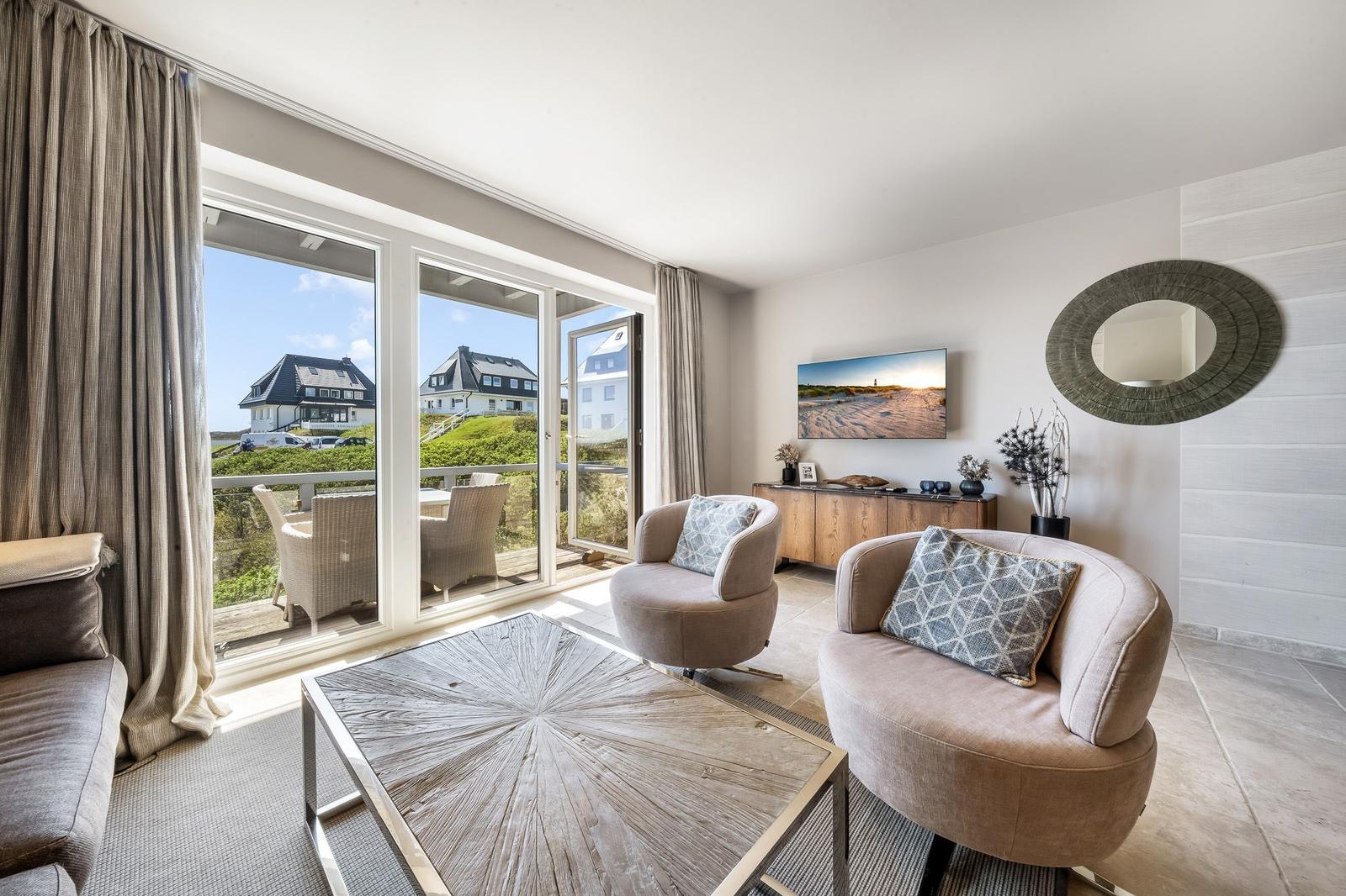 Wohnzimmer mit Blick auf Terrasse und Häuser. Möbel und Fernseher sind sichtbar.