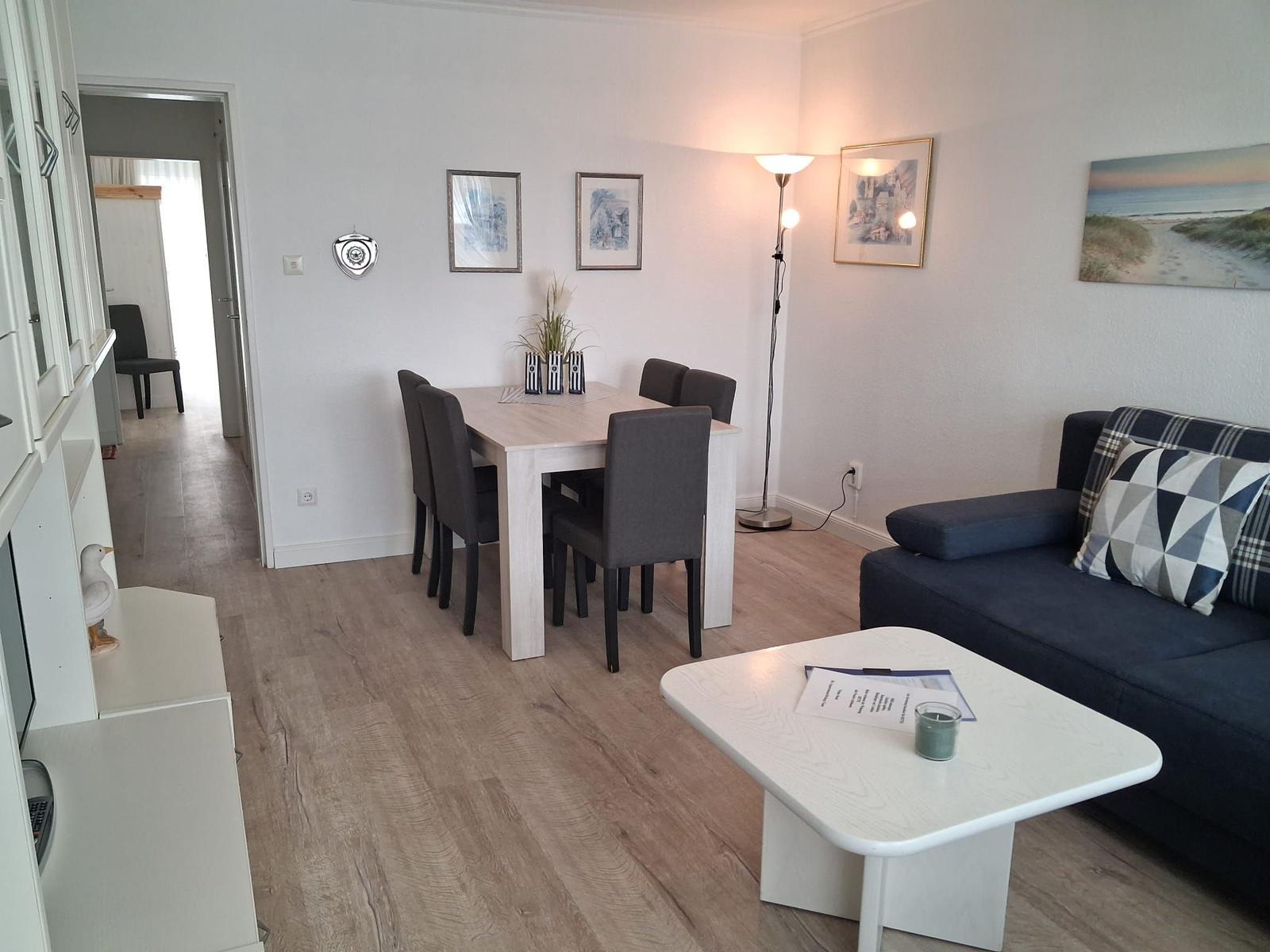Wohn- und Essbereich mit Sofa, Tisch und Stühlen. Holzboden und Wandbilder.