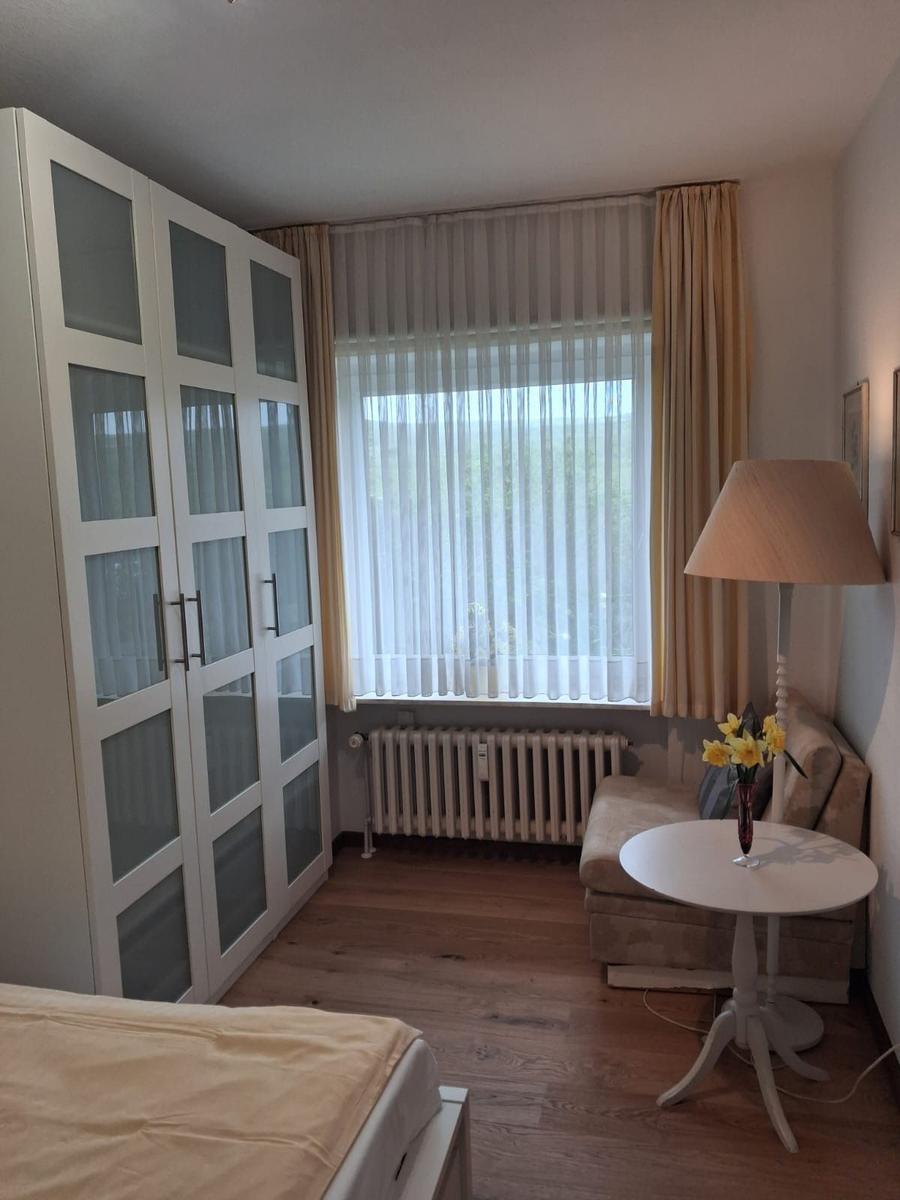 Bedroom with wardrobe, window, armchair, and table.