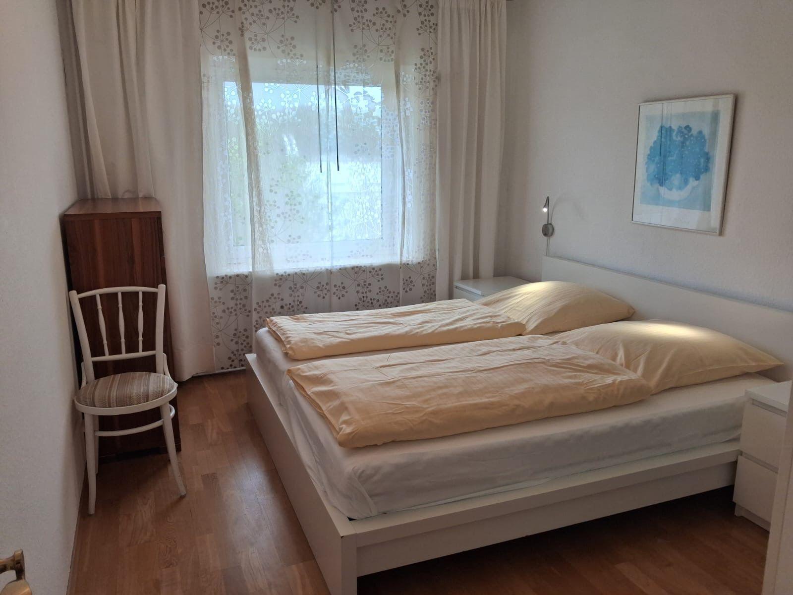Bedroom with double bed, window with curtains, and chair.