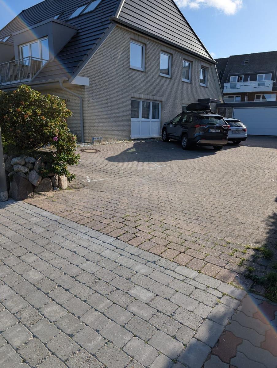 House with paved courtyard and two parked cars under blue sky.