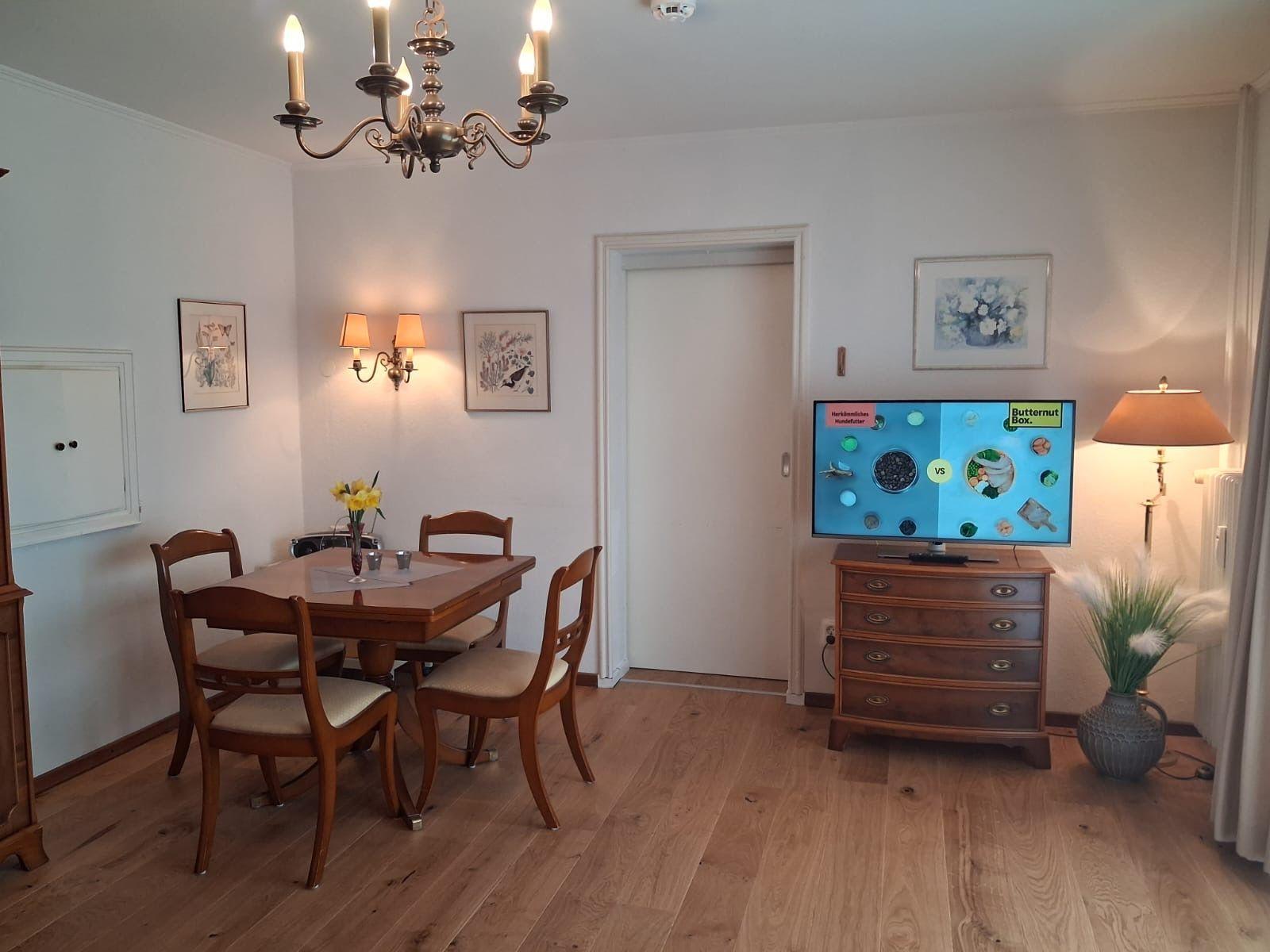 Dining room with wooden table, chairs, and TV on dresser. Chandelier and wall art.