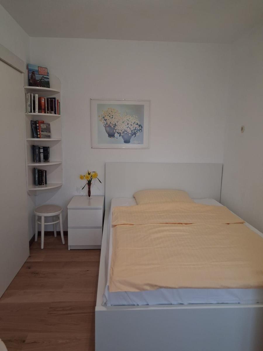 Bedroom with bed, nightstand, stool, and bookshelf on the wall.