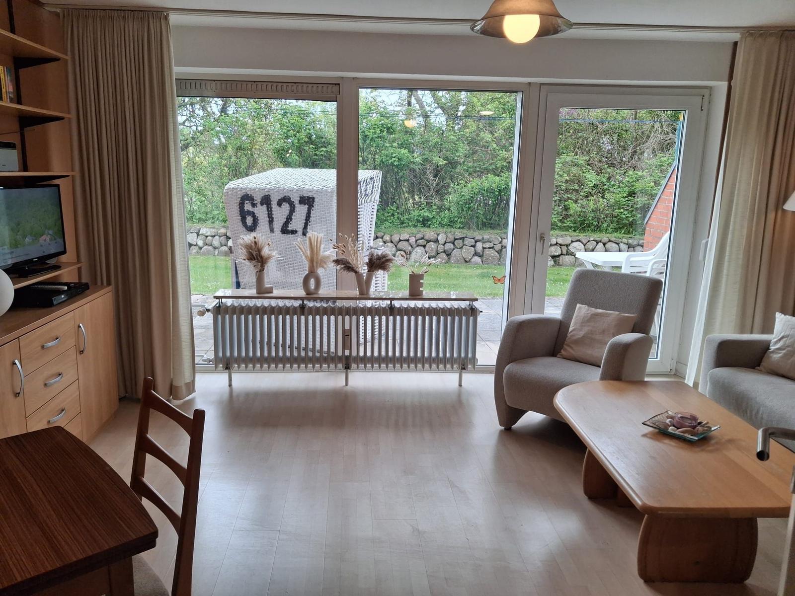 Wohnzimmer mit Blick auf Garten, Sitzgelegenheiten und Fernseher.