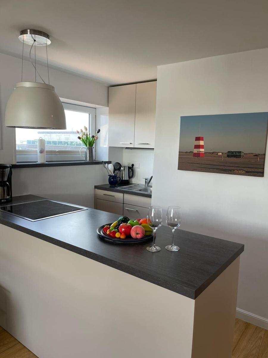 Küche mit Kücheninsel, Obst und Weinflaschen. Wandbild zeigt Leuchtturm.