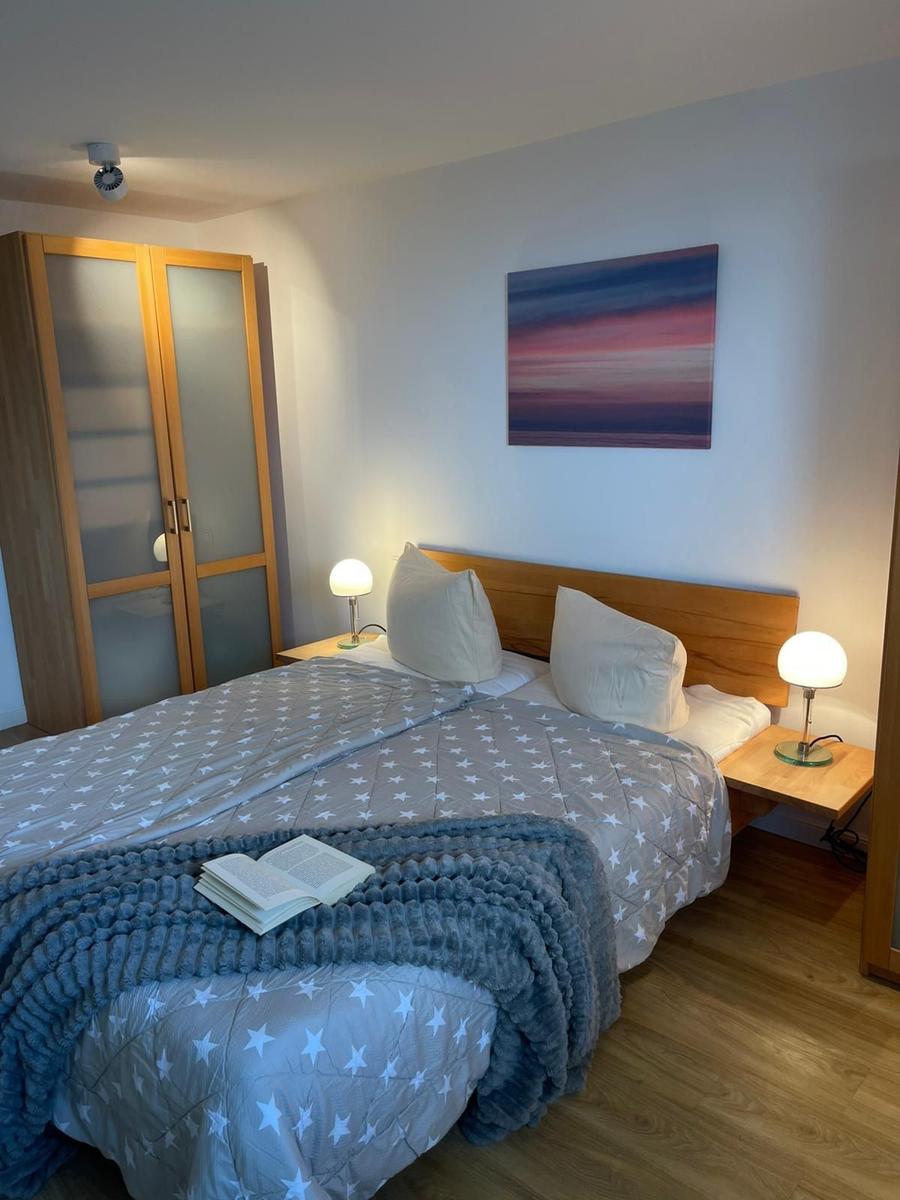 Ein Schlafzimmer mit Bett, Nachttischen und Lampen. An der Wand hängt ein Bild.