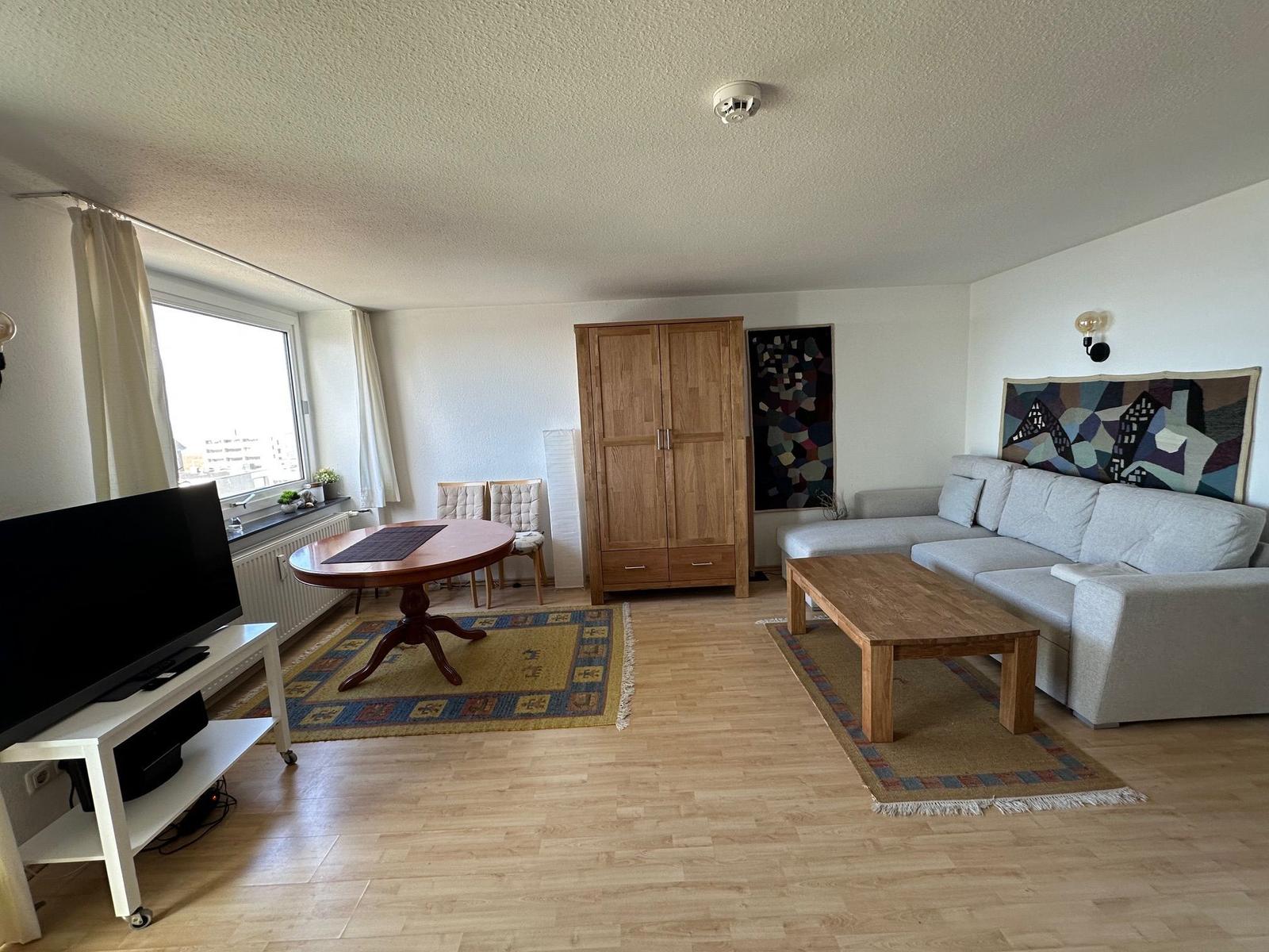 Wohnzimmer mit Sofa, Esstisch, Kleiderschrank und Fernseher.