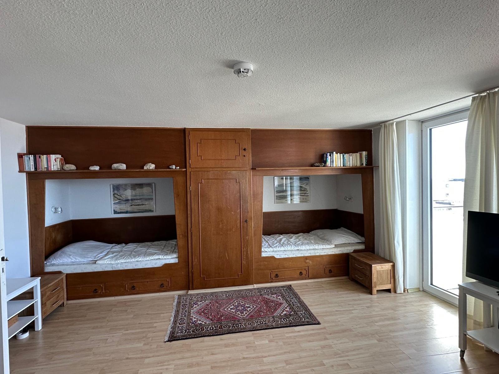 Zwei Schlafstellen mit Holzbetten, Bücherregale und ein Fenster.