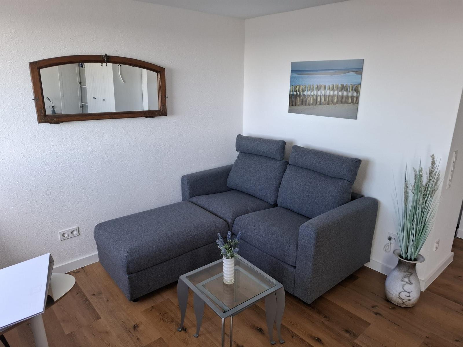Ein Wohnzimmer mit grauem Sofa, Glas-Tisch und Wandspiegel.