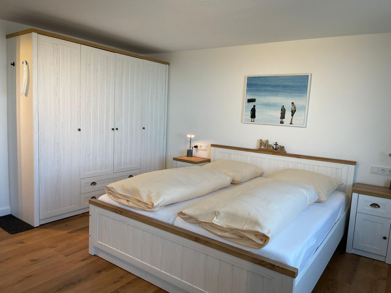 Schlafzimmer mit Doppelbett, Kleiderschrank und Nachttisch. Wandbild mit Strandmotiv.