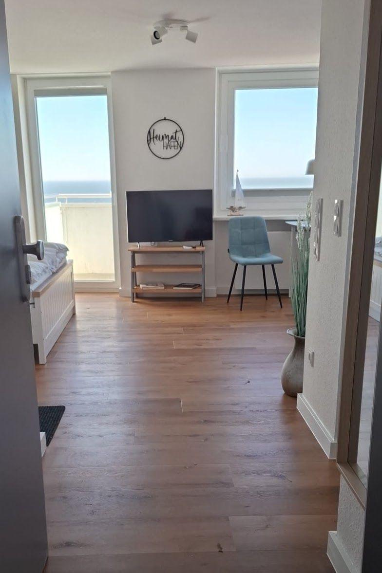 Wohnraum mit TV, Stuhl und Blick aufs Meer. Holzboden und große Fenster.