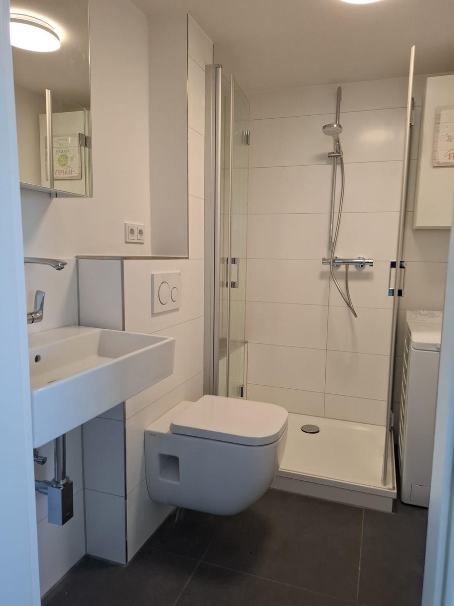 Badezimmer mit Dusche, WC und Waschbecken. Fliesenboden und Spiegelschrank.