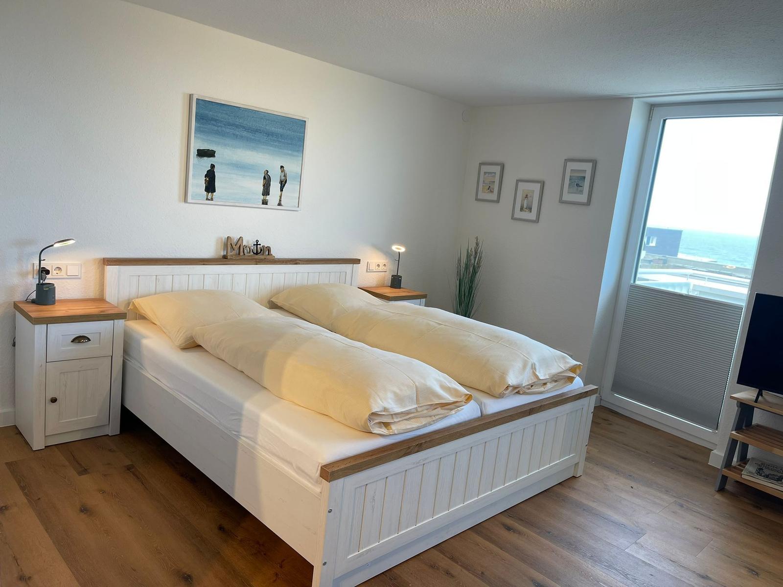 Schlafzimmer mit Doppelbett, Nachttischen und Meerblick durch Fenster.