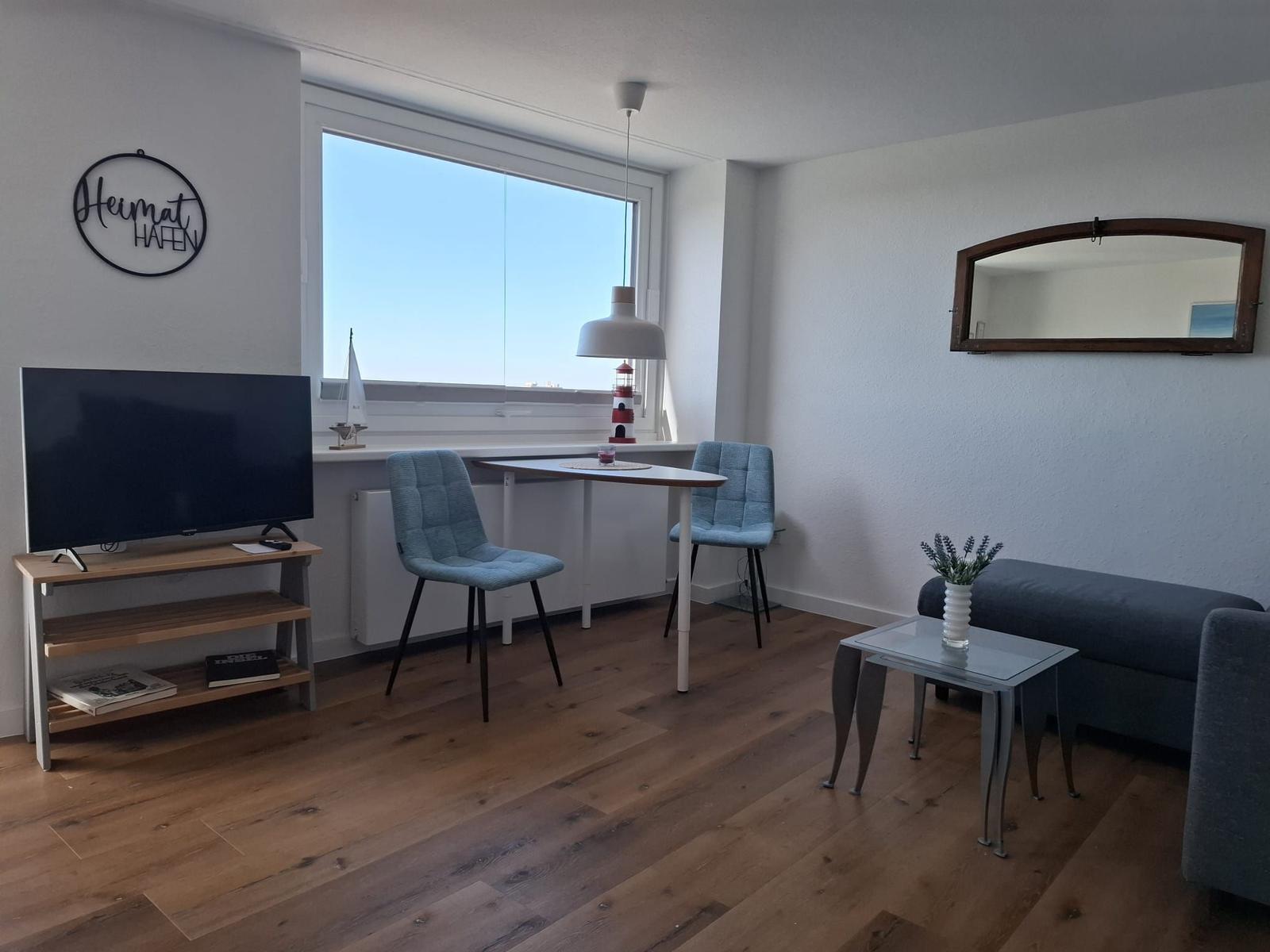 Wohnraum mit TV, Esstisch, Sofa und großem Fenster mit Hafenblick.