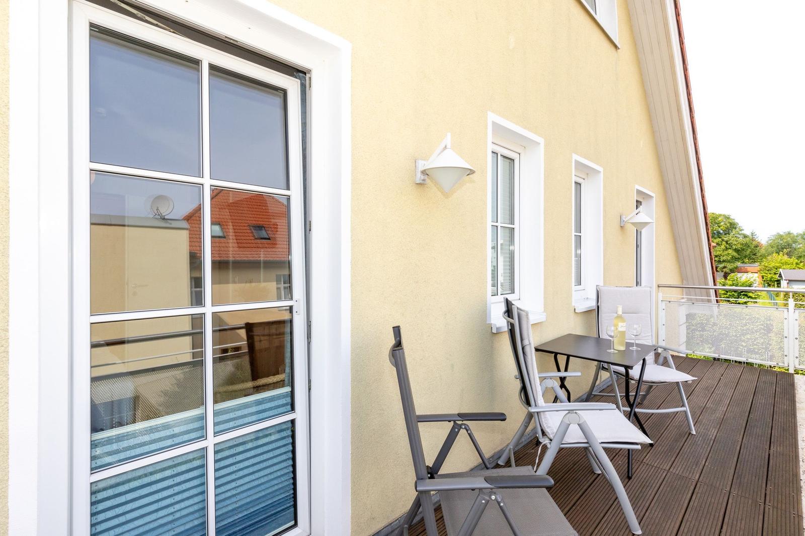 Terrasse mit Tisch, Stühlen und Flasche. Gelber Hauswandschutz mit Fenstern.