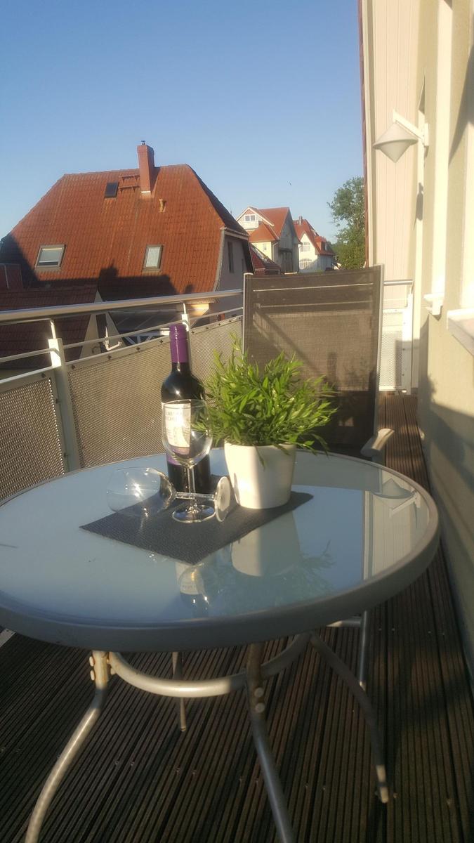 Terrasse mit Tisch, Stuhl, Weinflasche und Pflanze. Blick auf rote Dächer.
