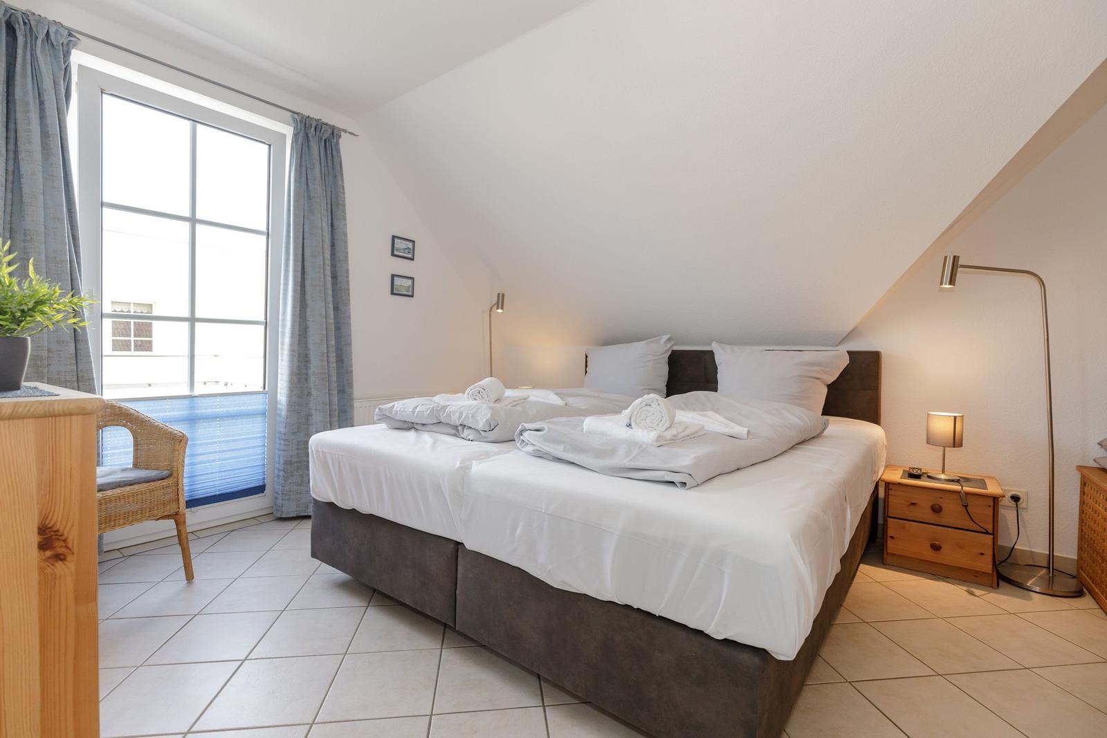 Schlafzimmer mit Doppelbett, Fenster und Nachttisch.