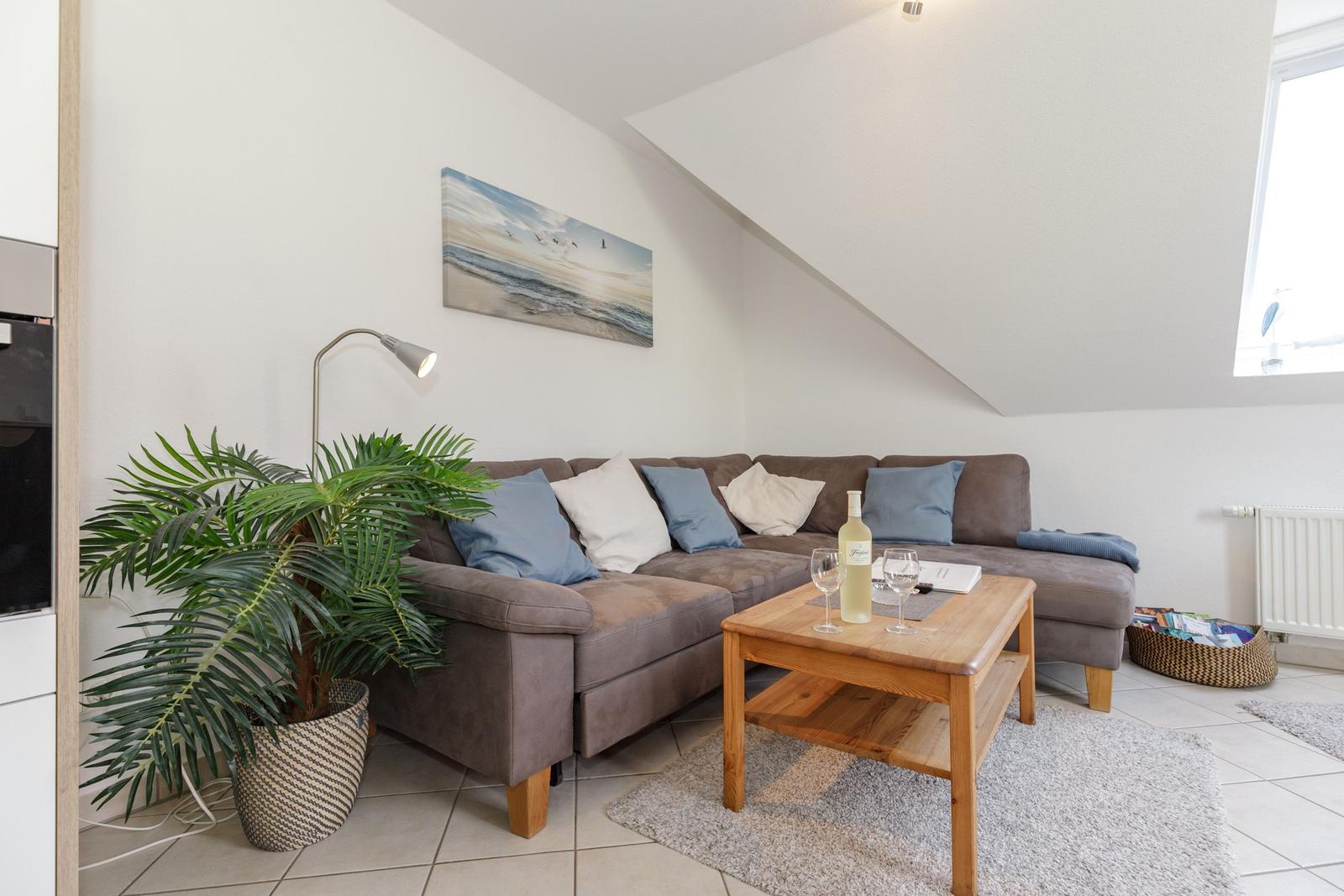 Wohnzimmer mit Sofa, Couchtisch und Pflanze unter schrägem Dach