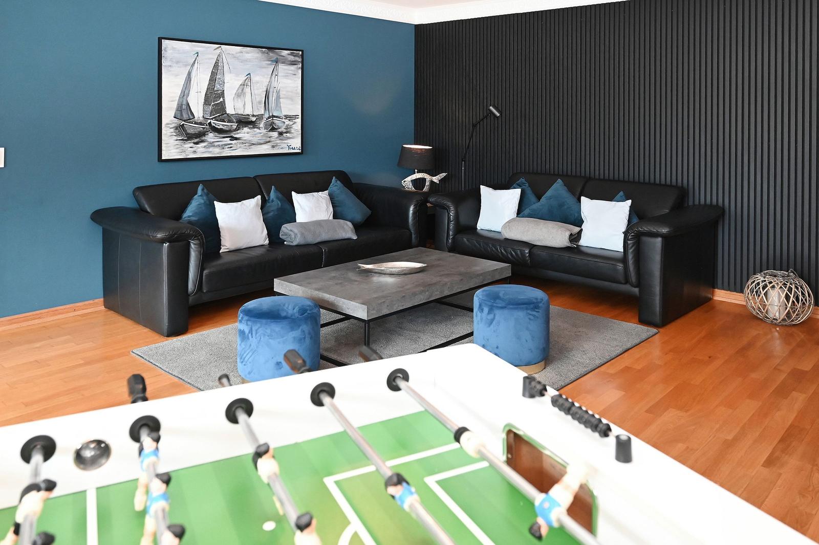 Wohnzimmer mit zwei Sofas, Tisch und Fussballtisch. Wand mit Segelboot-Bild.