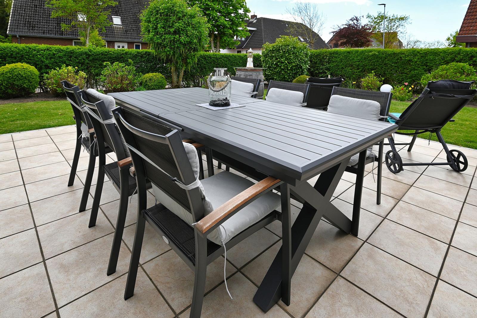 Gartenbereich mit gedecktem Tisch und Stühlen auf Terrasse.