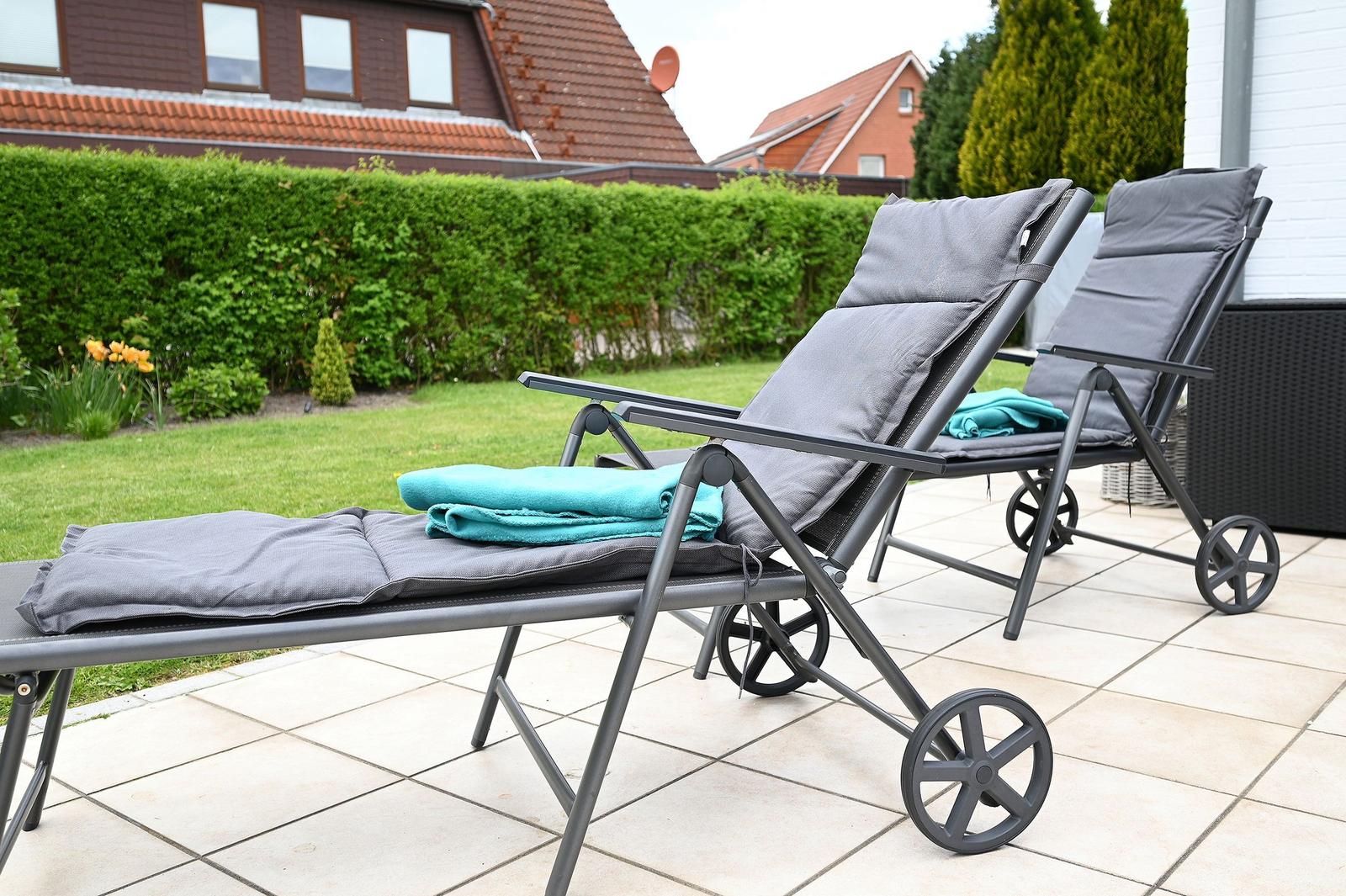 Zwei Liegestühle mit Kissen und Handtüchern auf einer Terrasse mit Rasen und Hecke im Hintergrund.