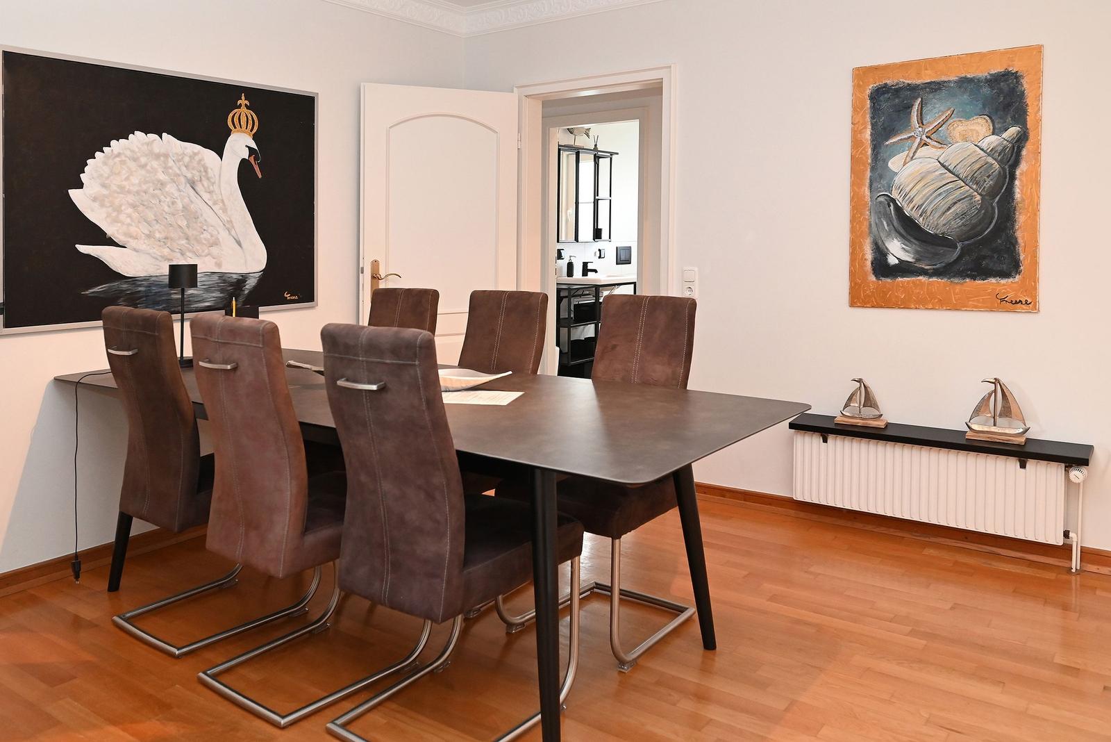 Esszimmer mit Holzboden, Esstisch und sechs Stühlen. Wandbilder und Modellboote.