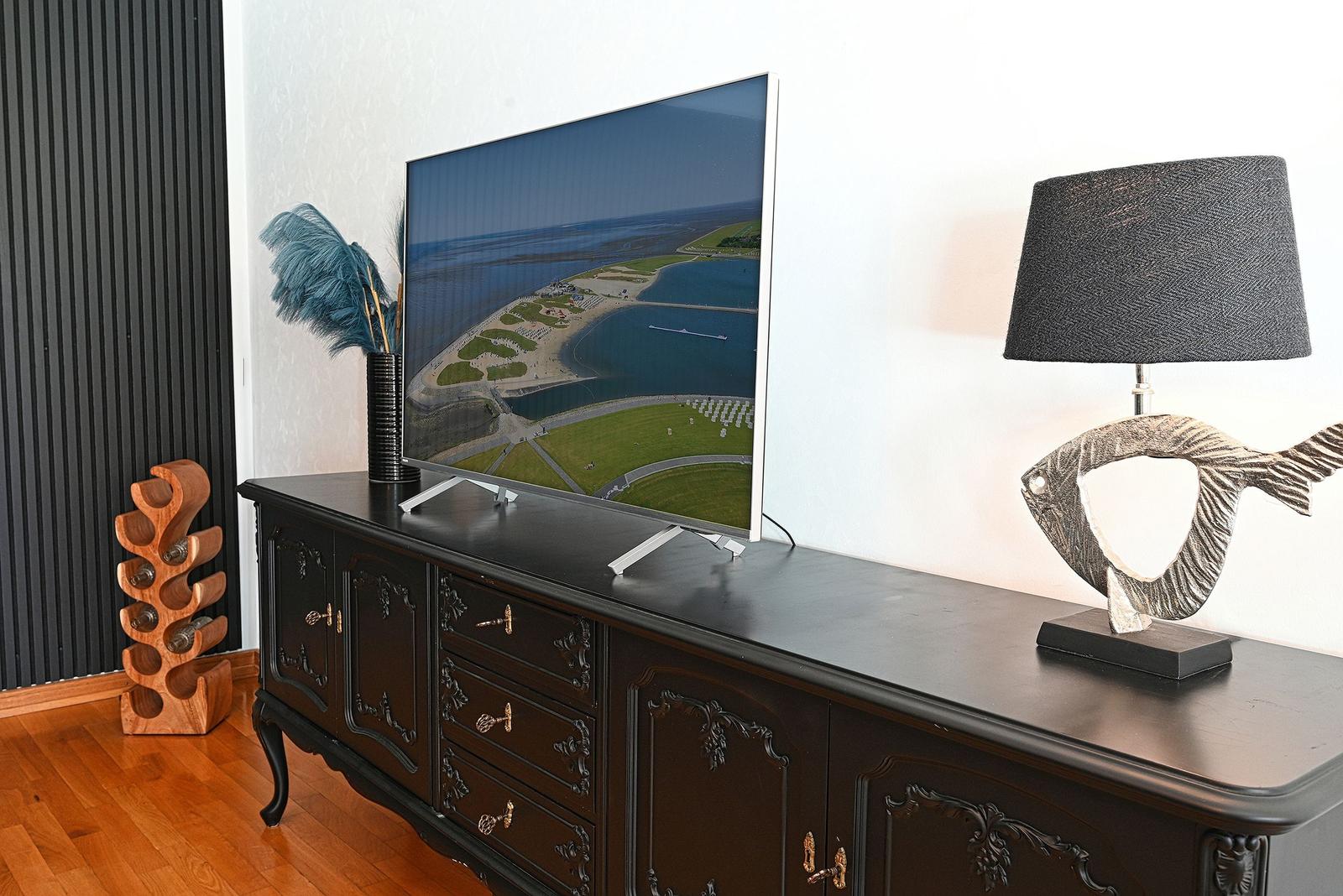 TV auf dunklem Sideboard mit Fischlampe und Flaschenhalter
