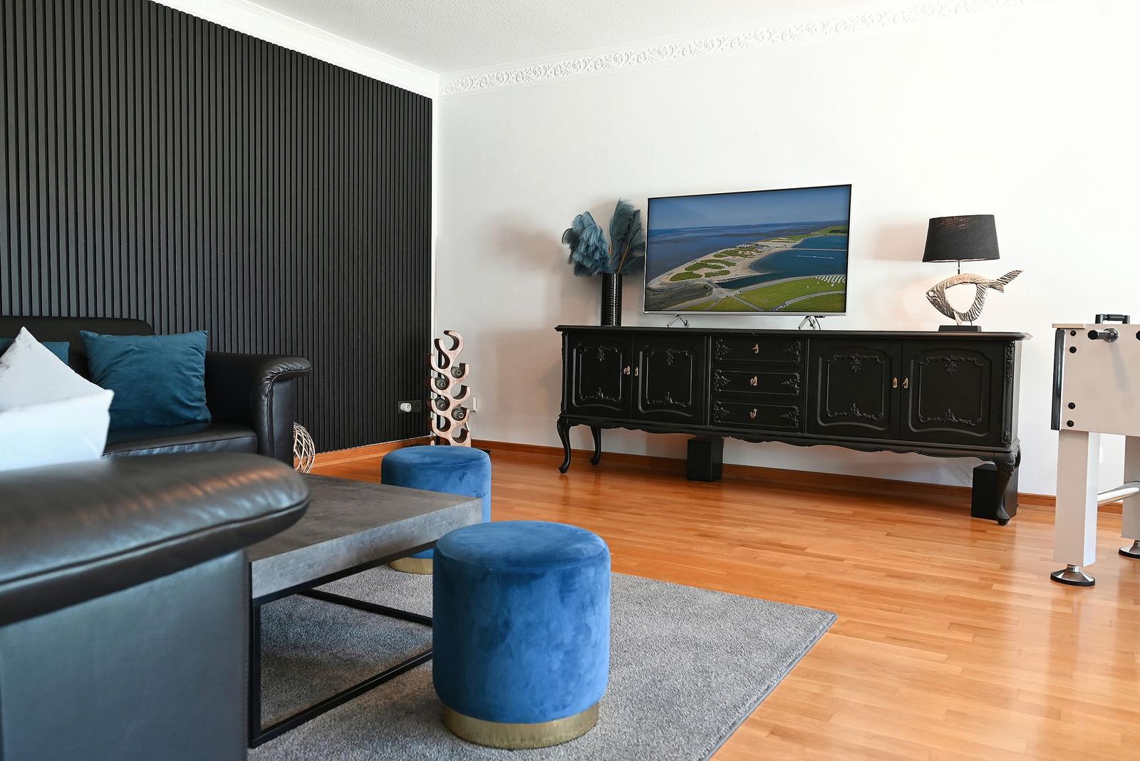 Wohnzimmer mit Sofa, blauen Sitzkissen und Fernseher auf Sideboard.