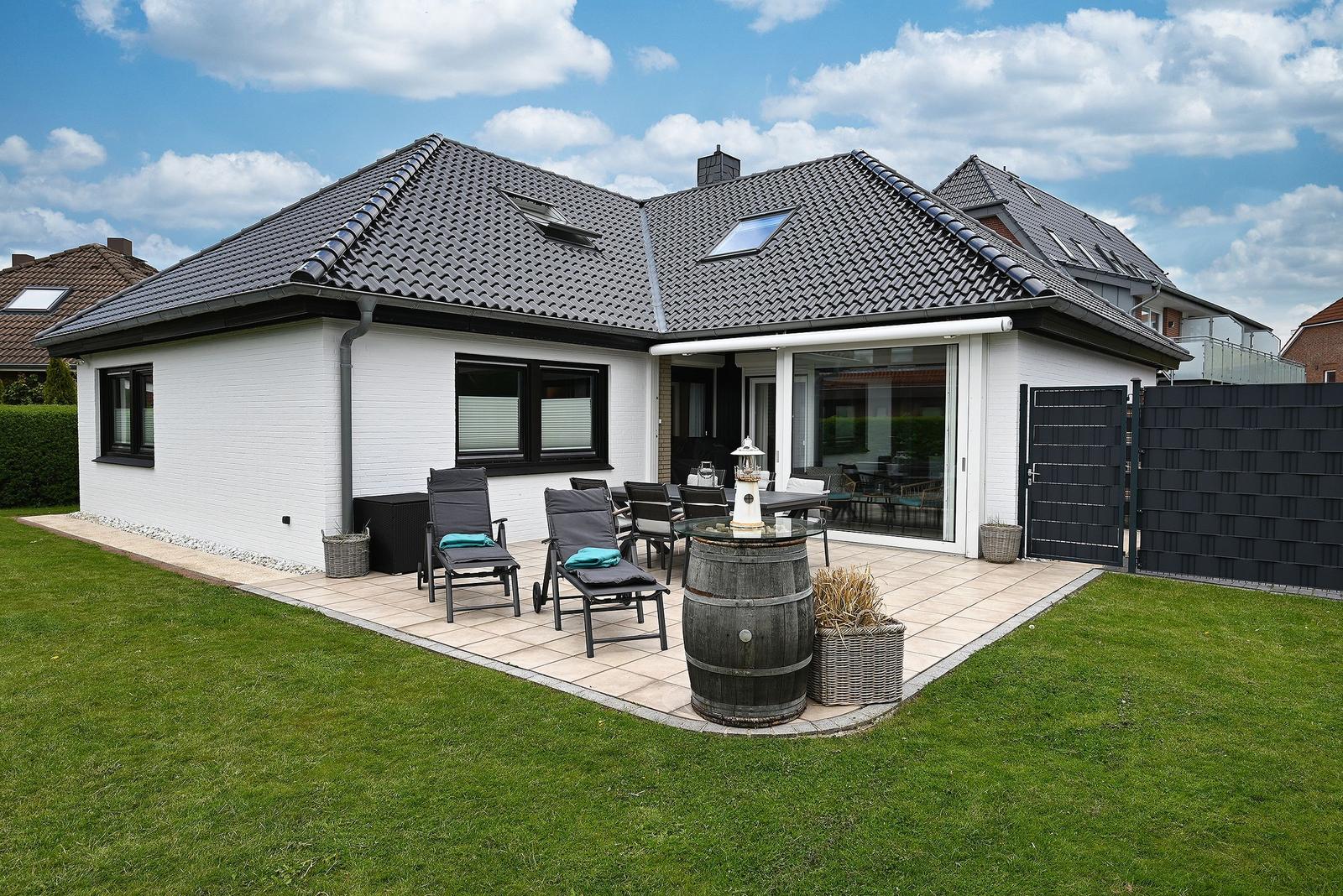 Wohnhaus mit Terrasse, Garten und Sitzgelegenheiten. Schwarzes Dach und weiße Fassade.