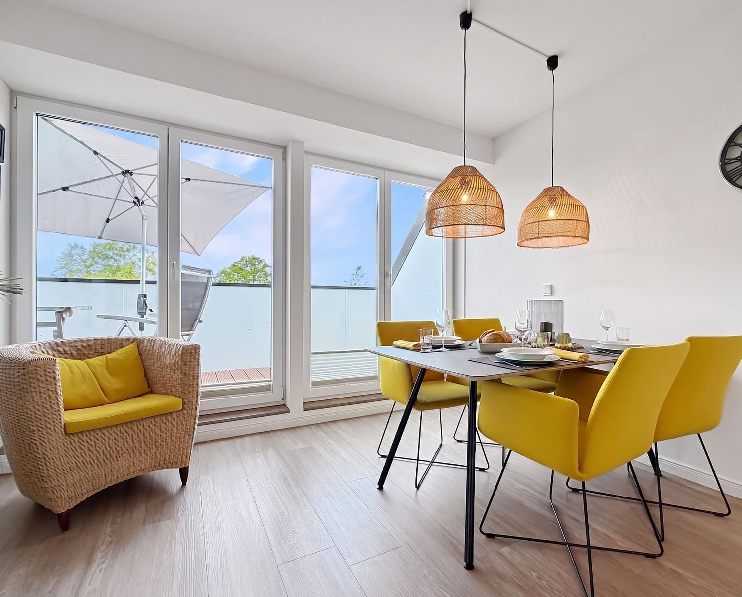 Essbereich mit gelben Stühlen und Tisch. Balkon mit Sonnenschirm und Gartenmöbeln.