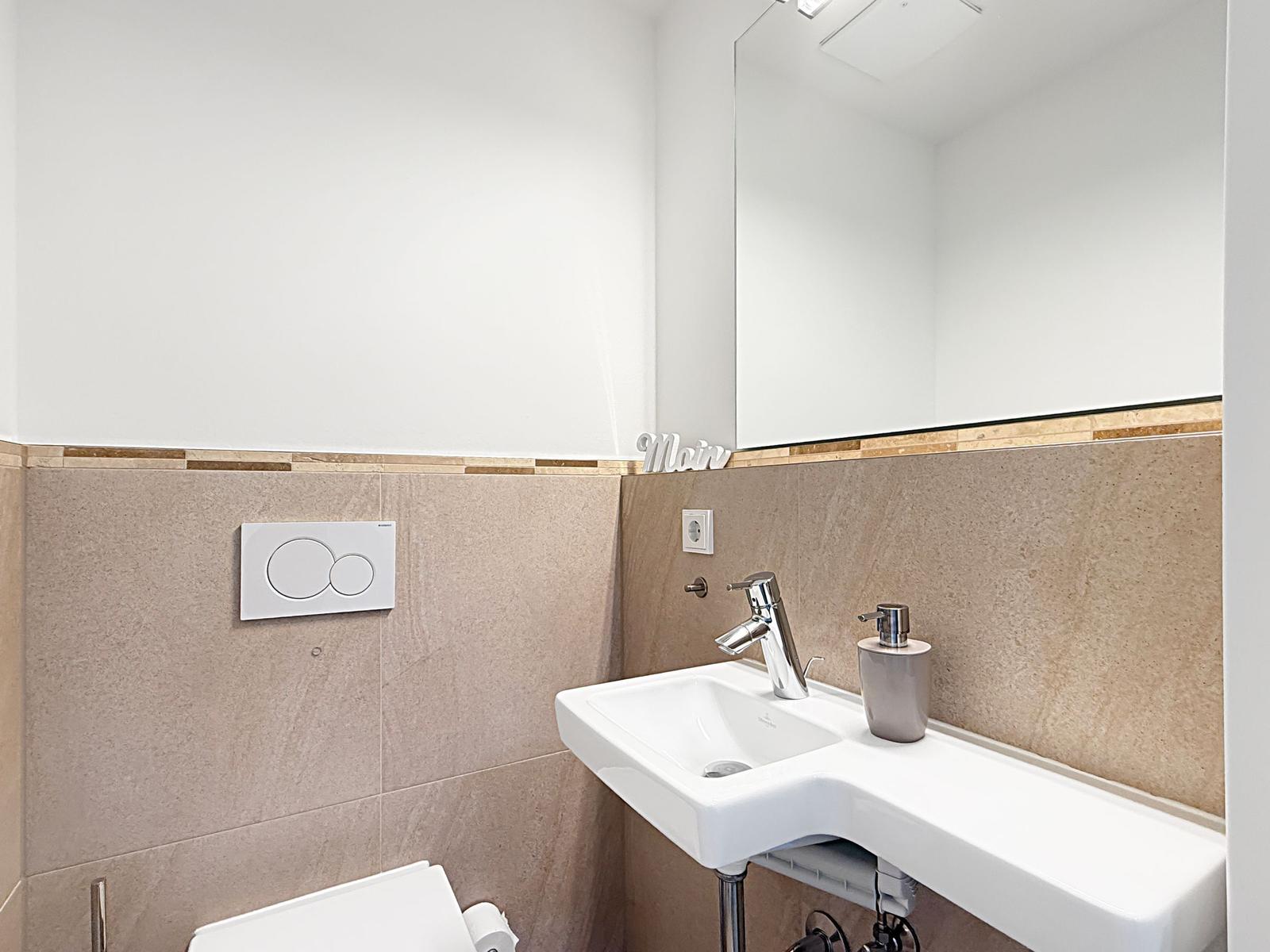Badezimmer mit Waschbecken, Spiegel und Toilette.