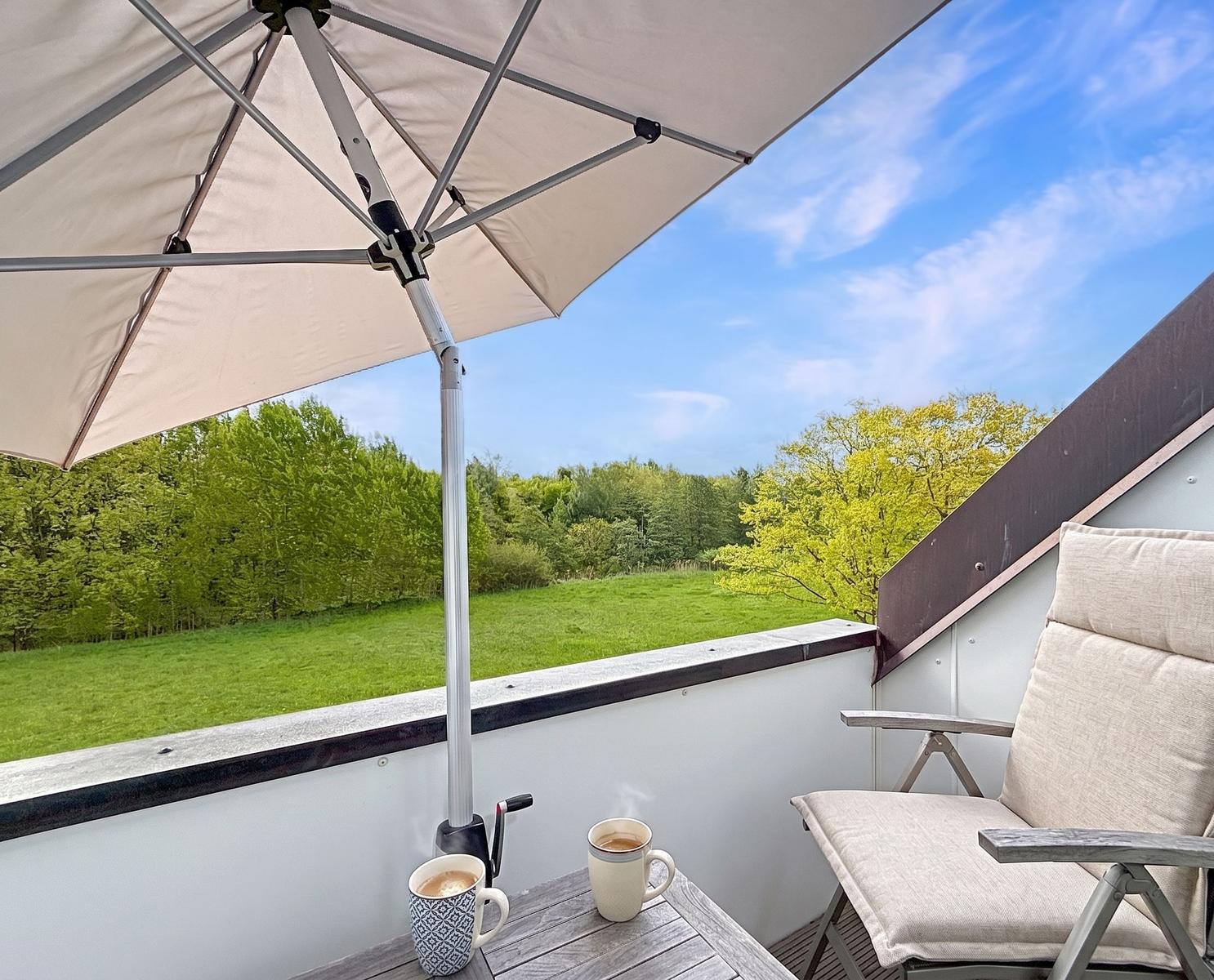 Terrasse mit Sonnenschirm, Tisch und Stuhl. Blick auf grünes Feld und Bäume.