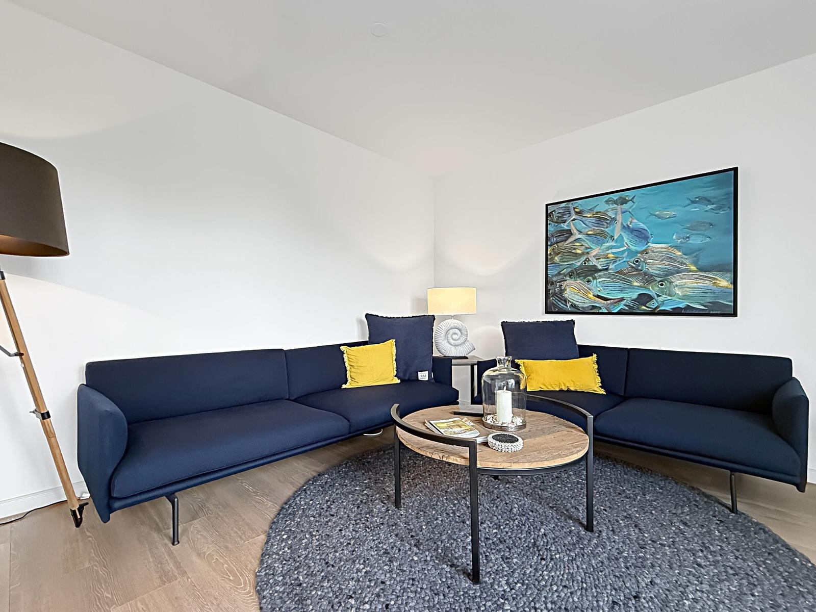 Ein Wohnzimmer mit blauem Sofa, runden Tisch und Wandbild mit Fischen.