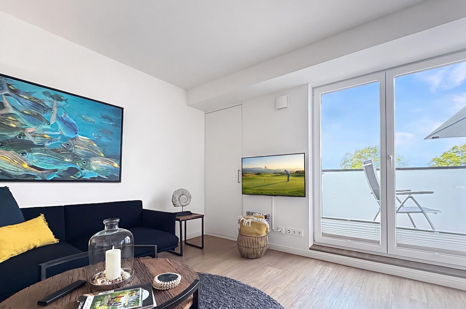 Wohnzimmer mit Sofa, Fernseher und Balkonansicht.