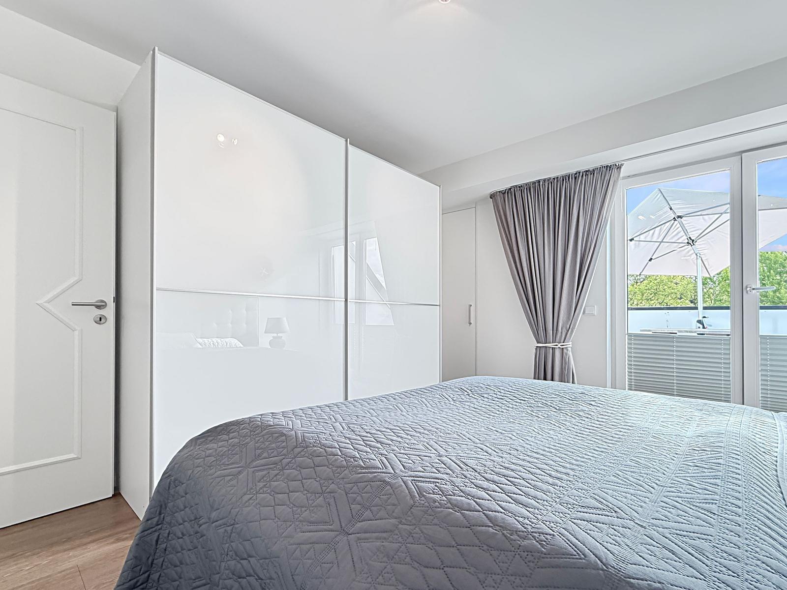 Schlafzimmer mit Bett, Schrank und Balkon mit Sonnenschirm.