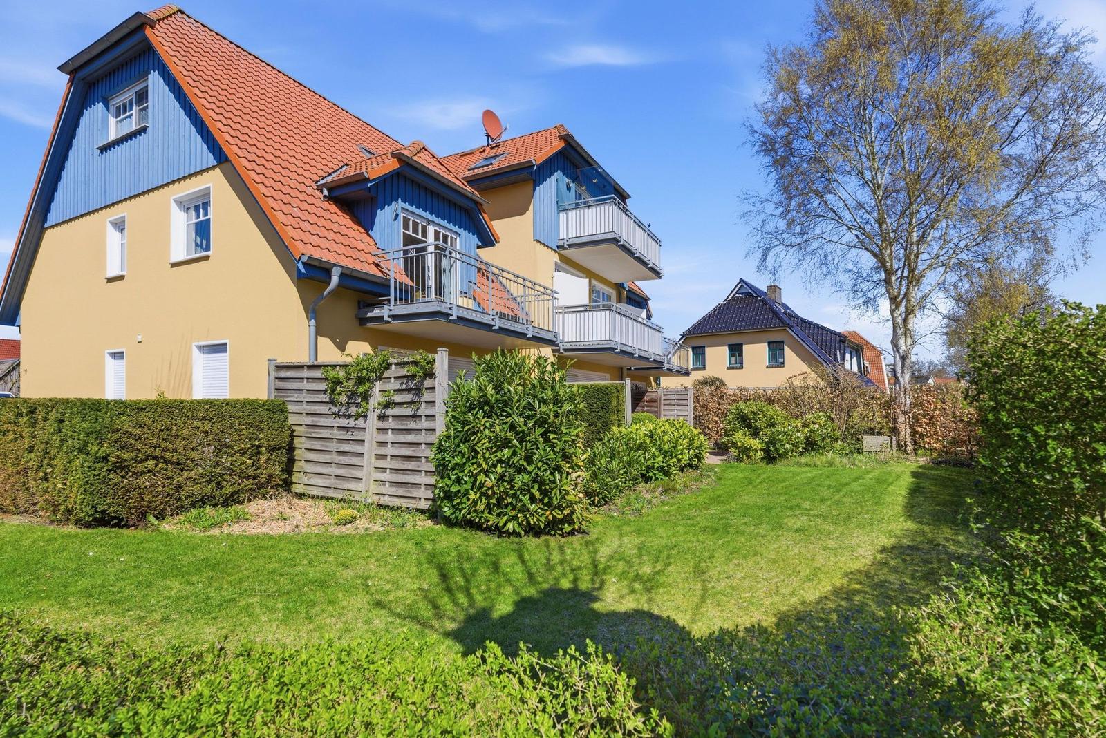 Haus mit Balkonen und Garten. Roter Dachfirst und blau-gelbe Fassade.