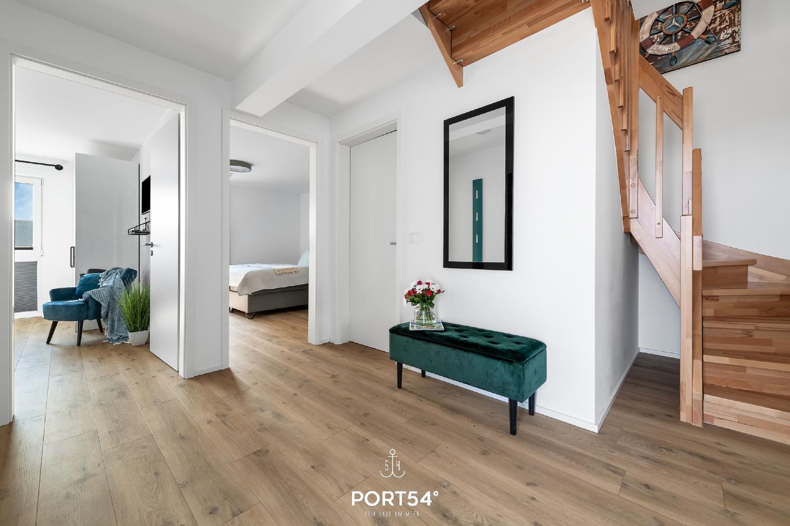 Eingangsbereich mit grünem Sitzbank, Spiegel und Holztreppe. Durchgänge zu Schlaf- und Wohnbereich.