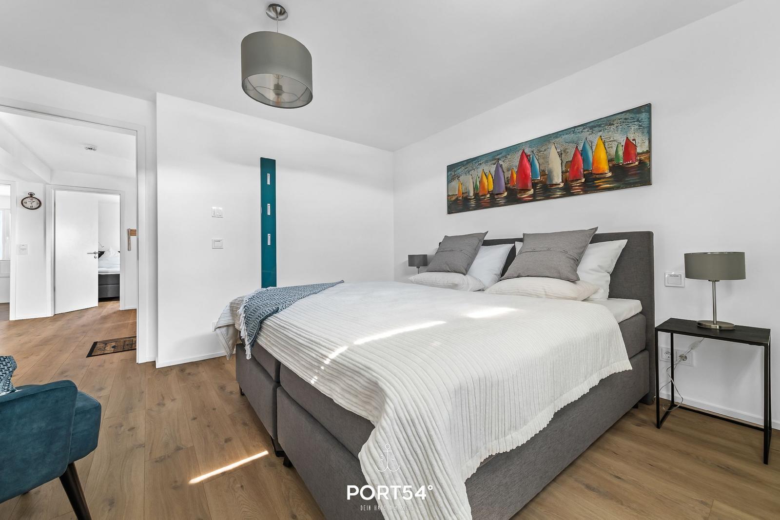 Schlafzimmer mit Bett, Wandbild und Nachttisch. Holzboden und Deckenleuchte.