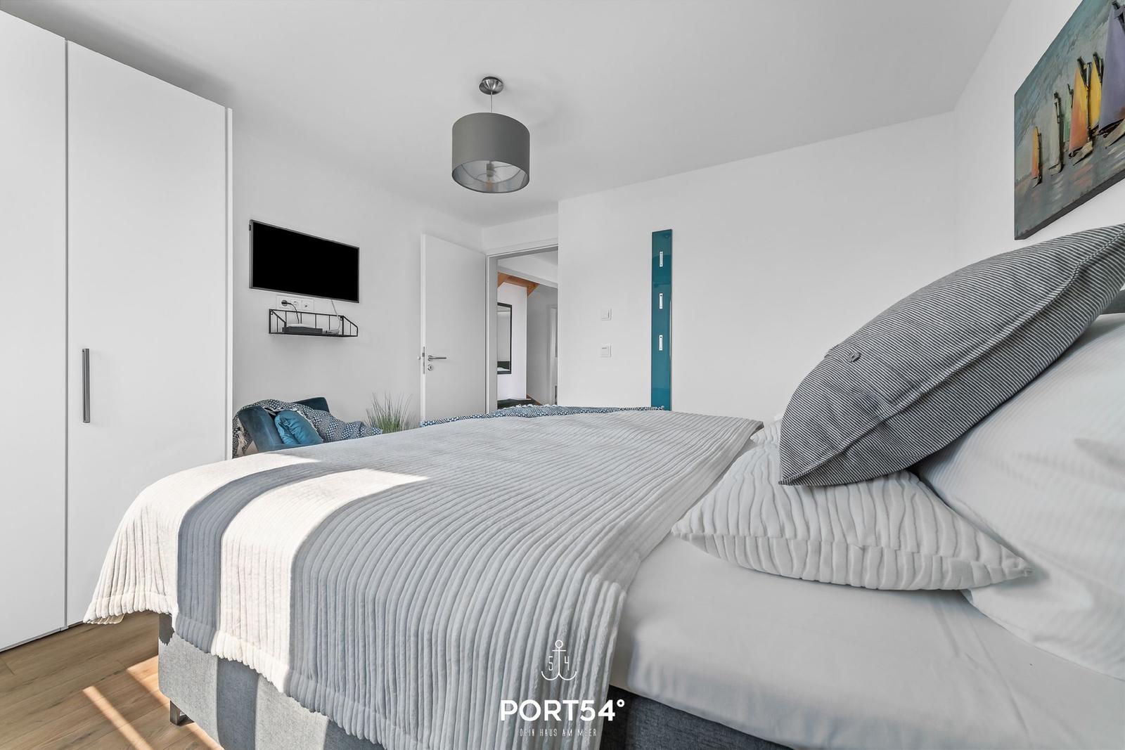 Schlafzimmer mit Bett, Kleiderschrank und Fernseher an der Wand.