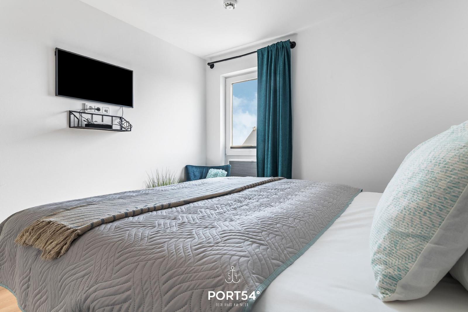 Schlafzimmer mit Bett, Fenster und Wandfernseher.